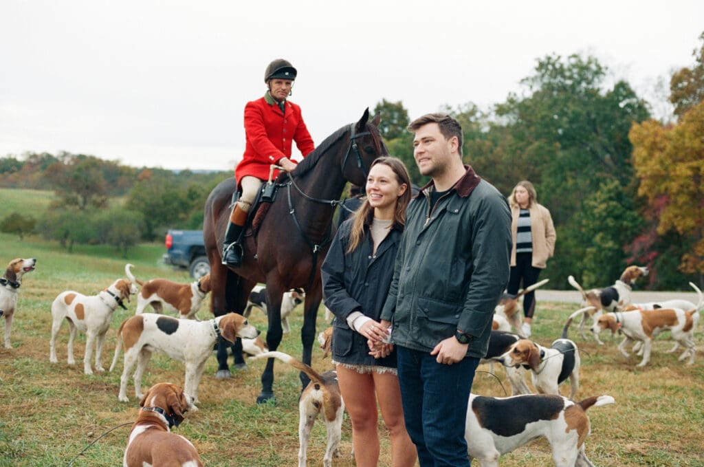Bride and groom stand amongst hound dogs with a red-coated horseback rider behind them